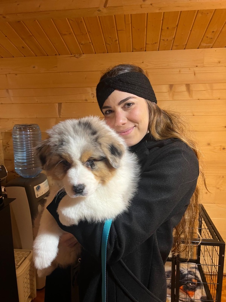 Daniela holding Blue, a blue merle Australian Shepherd puppy, inside a wooden cabin